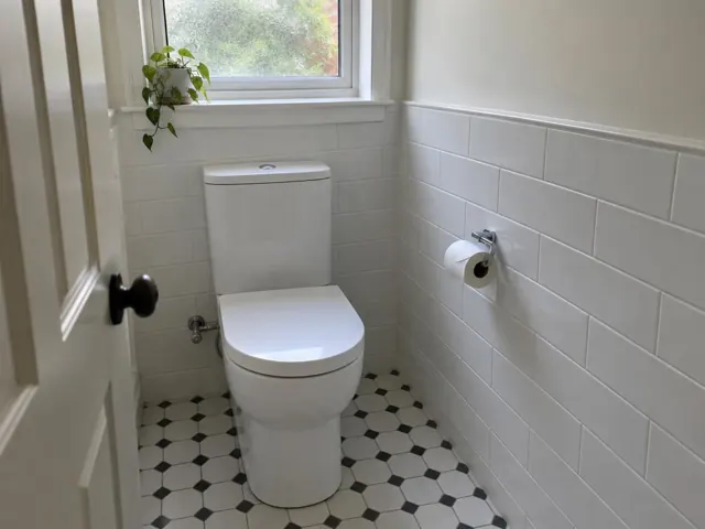 Clean white toilet in a tiled bathroom with a window and open door in Strathfield