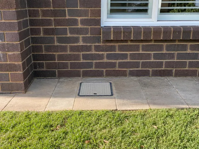 Flush capped inspection opening in tiled patio beside a brick house wall in Burwood